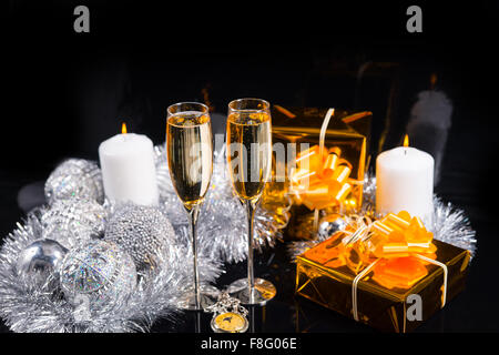 Festa di Natale scintillante ancora in vita - Orologio da tasca, bicchieri di champagne, regali avvolti in carta oro, candela con la fiamma e decorazioni color argento su sfondo nero. Foto Stock