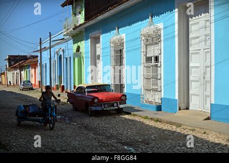 Moto d'epoca e lato guida auto sulla pavimentazione passato un rosso parcheggiate auto d'epoca, Trinidad Sancti Spiritus Provincia Cuba Foto Stock