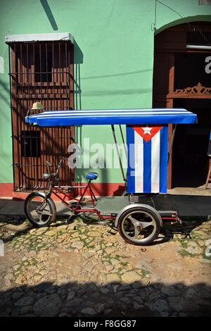 Ciclo cubano taxi con bandiera cubana come baldacchino del sole parcheggiata su una soleggiata strada di ciottoli in Trinidad, Cuba Foto Stock