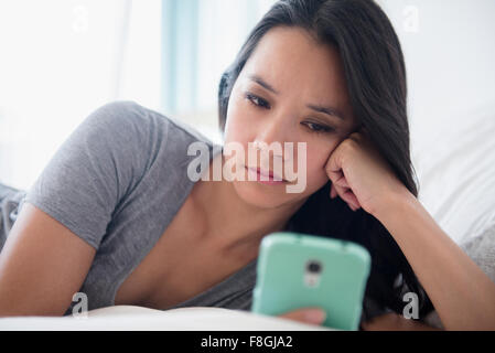 Donna cinese tramite telefono cellulare sul letto Foto Stock