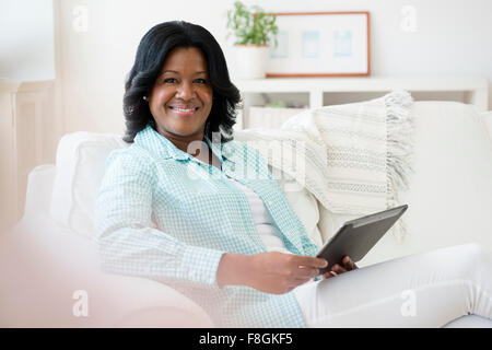 Donna nera con tavoletta digitale sul divano Foto Stock