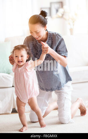 Madre aiutare la nostra bambina a piedi in salotto Foto Stock