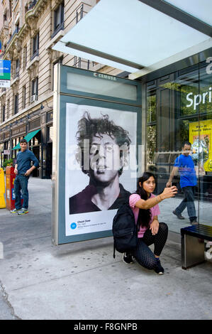 Una giovane donna assume un selfie con un Chuck Close pittura riprodotta su un pannello pubblicitario in un rifugio di autobus nella città di New York durante l'arte ovunque evento. Foto Stock