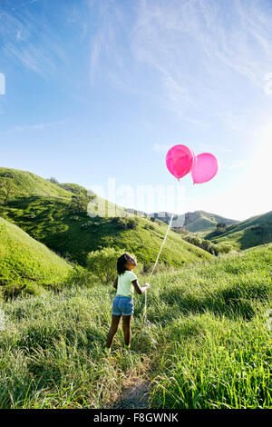 Ragazza nera con palloncini sulla collina rurale Foto Stock