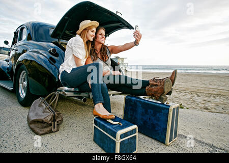 Le donne con i bagagli e auto d'epoca, sulla spiaggia Foto Stock