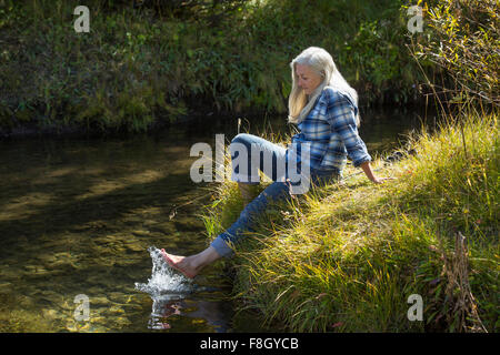 La donna caucasica schizzi piedi nel fiume Foto Stock