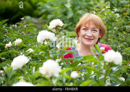 Donna matura in pioni impianto in giardino Foto Stock