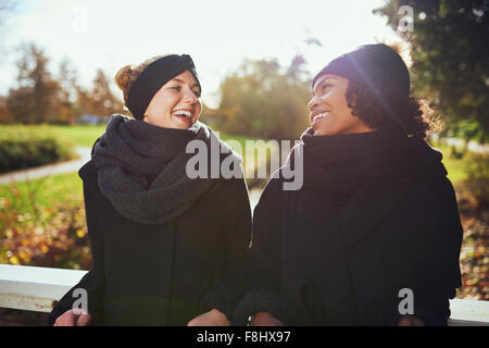 Due donne in vestiti caldi in piedi sul ponte in park e sorridente ad ogni altro Foto Stock