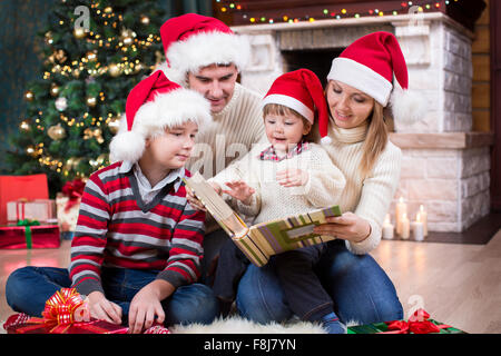 Famiglia rivedendo le loro foto in album vicino a albero di Natale di fronte al caminetto Foto Stock