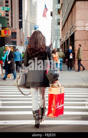 NEW YORK CITY - 4 dicembre 2015: Donna attraversa street nel centro di Manhattan con una Macy's shopping bag durante la vacanza di Natale Foto Stock