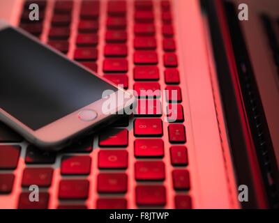 Angolo di Alta Vista del telefono cellulare sulla tastiera del computer in illuminazione rossa Foto Stock