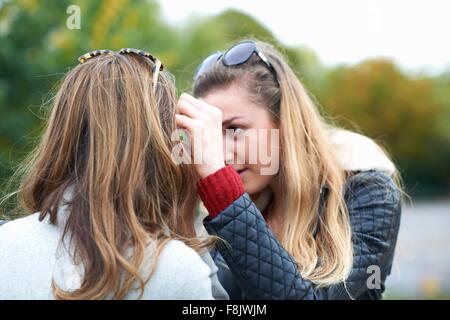 Giovane donna spazzolare i capelli da amico del viso, vista posteriore Foto Stock