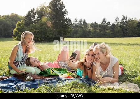 Le donne che giace su fronti di erba utilizza lo smartphone per prendere selfie sorridente Foto Stock