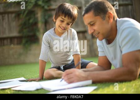 Ragazzo seduto sull'erba la visione di padre fare carte guardando giù sorridente Foto Stock