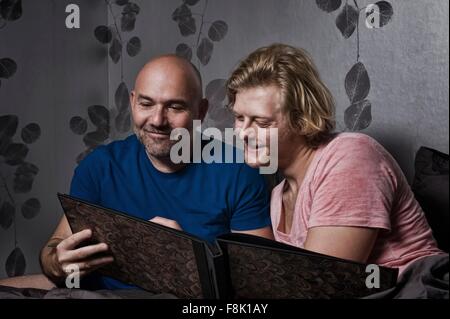 Voce maschile giovane seduto a letto guardando album di foto Foto Stock