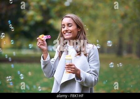 Giovane donna a soffiare bolle in autunno park Foto Stock