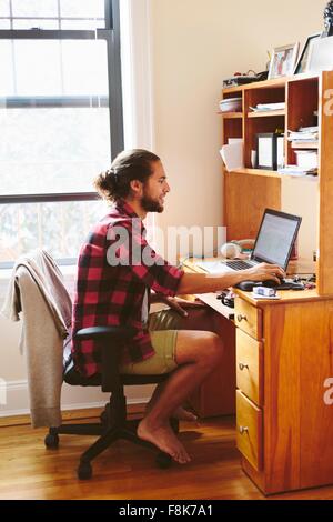 Giovane uomo seduto alla scrivania, utilizzando laptop Foto Stock