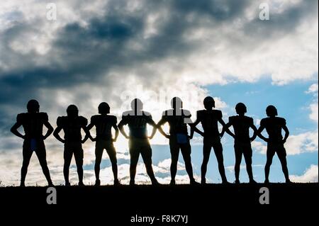 Silhouette di un gruppo di giovani american football giocatori, in piedi in fila, le mani sui fianchi Foto Stock