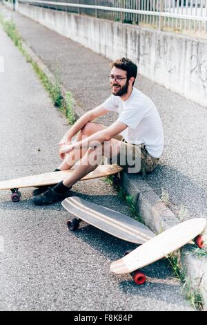 Giovane uomo seduto sul cordolo con tre skateboard Foto Stock