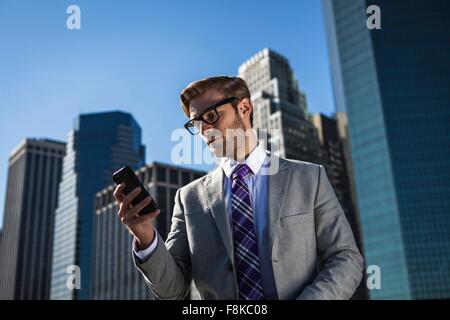 Giovane imprenditore di fronte all edificio per uffici la lettura di testi di smartphone, New York, Stati Uniti d'America Foto Stock