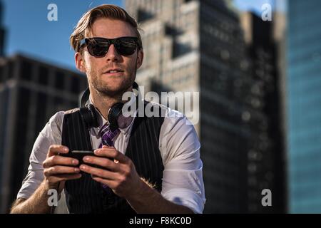 Giovane imprenditore nel front office che guarda lontano mentre utilizza lo smartphone, New York, Stati Uniti d'America Foto Stock