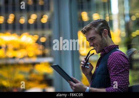 Felice giovane impreditore appoggiata contro la finestra del parco la lettura digitale compressa Foto Stock