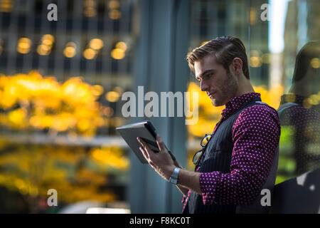 Giovane imprenditore appoggiata contro la finestra del parco la lettura digitale compressa Foto Stock