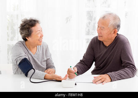 Felice coppia Senior tenendo la pressione sanguigna in salotto Foto Stock