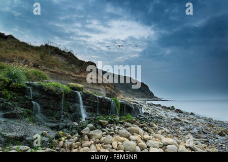 Immagine orizzontale di una cascata che scorre sulla spiaggia rocciosa di sunrise Foto Stock