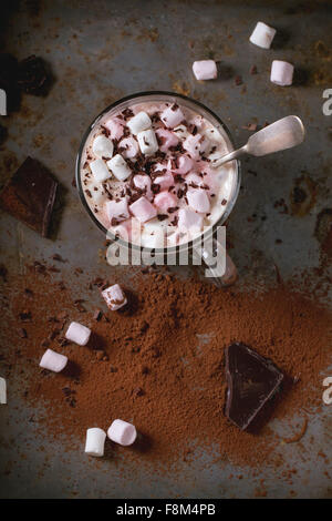 Vetro tazza di cioccolata calda con fusione marshmallows, vintage cucchiaio d'argento e la polvere di cacao ruggine sulla superficie metallica. Rustico scuro Foto Stock