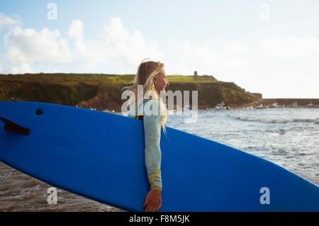 Surfista femmina camminando verso il mare, portando le tavole da surf Foto Stock