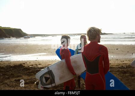 Gruppo di surfers permanente sulla spiaggia, tenendo le tavole da surf, vista posteriore Foto Stock