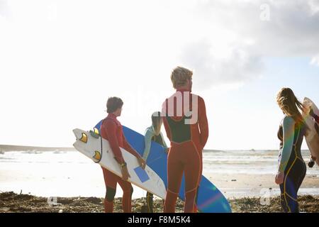 Gruppo di surfers permanente sulla spiaggia, tenendo le tavole da surf, vista posteriore Foto Stock