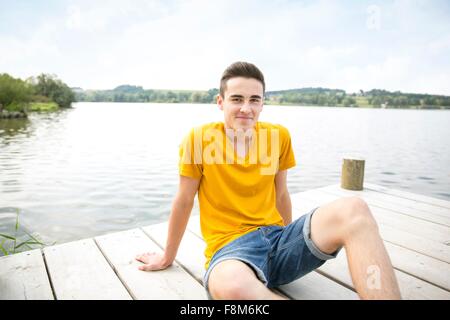 Ritratto di giovane uomo seduto sul molo Foto Stock