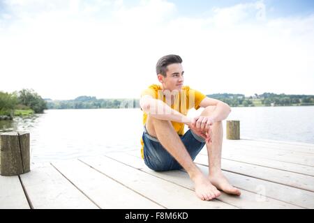 Ritratto di giovane uomo seduto sul molo Foto Stock