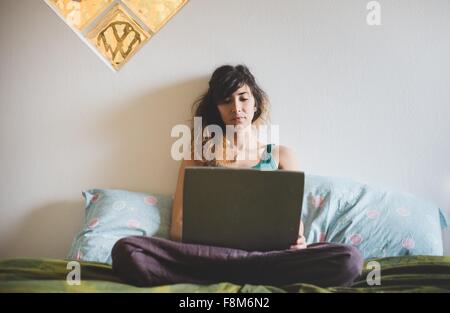 Vista frontale della metà donna adulta seduta zampe trasversale sul letto tramite computer portatile Foto Stock