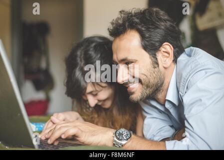 Testa e spalle di coppia giovane sdraiato sul lato anteriore utilizzando il computer portatile Foto Stock