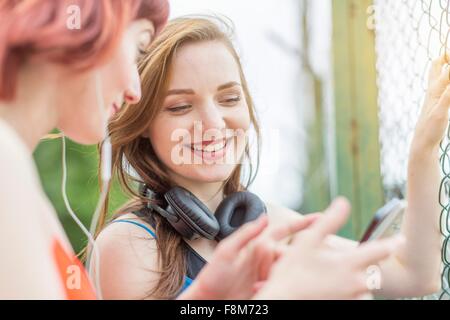 Giovani donne utilizza lo smartphone a fianco di recinzione Foto Stock