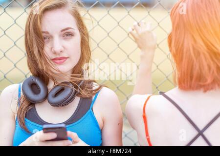 Giovane donna utilizza lo smartphone a fianco di recinzione Foto Stock