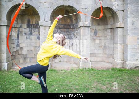 Giovane donna pratica di danza a nastro, archi murati in background Foto Stock