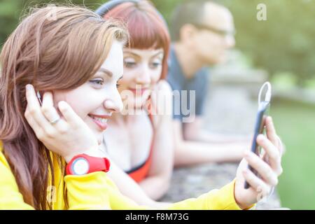 Giovani donne utilizza lo smartphone, appoggiata sulla parete bassa Foto Stock