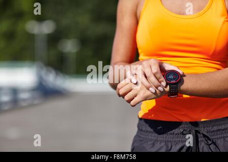 Ritagliato colpo di giovane femmina impostazione runner smartwatch in parcheggio Foto Stock