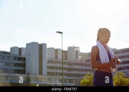 Giovani femmine runner controllo smartwatch sul tetto urbano Foto Stock