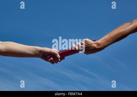 Le mani del relè femmina corridori passando il testimone contro il cielo blu Foto Stock