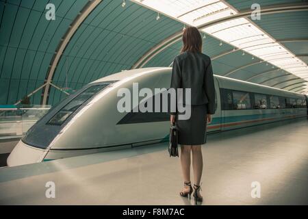 Business donna in attesa di un treno su piattaforma ferroviaria, Shanghai, Cina Foto Stock