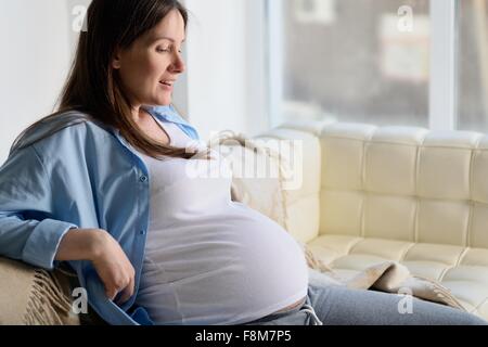 Donna incinta seduta sul divano Foto Stock