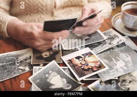 Senior donna seduta al tavolo, guardando attraverso le vecchie fotografie, metà sezione Foto Stock