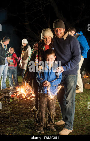 Little Boy giocando con un sparkler con i suoi genitori a guardare lui Foto Stock