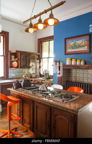 La casa dei designer Erica Pols. La cucina con funzione di blu parete. Ripiani e un'isola con armadi e arancione brillante Alessi sgabelli. Stile tradizionale cucina con porte in legno. Foto Stock