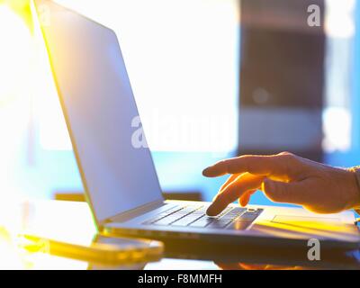 Imprenditore digitazione sul computer portatile in ufficio con la luce del sole proveniente attraverso la finestra Foto Stock